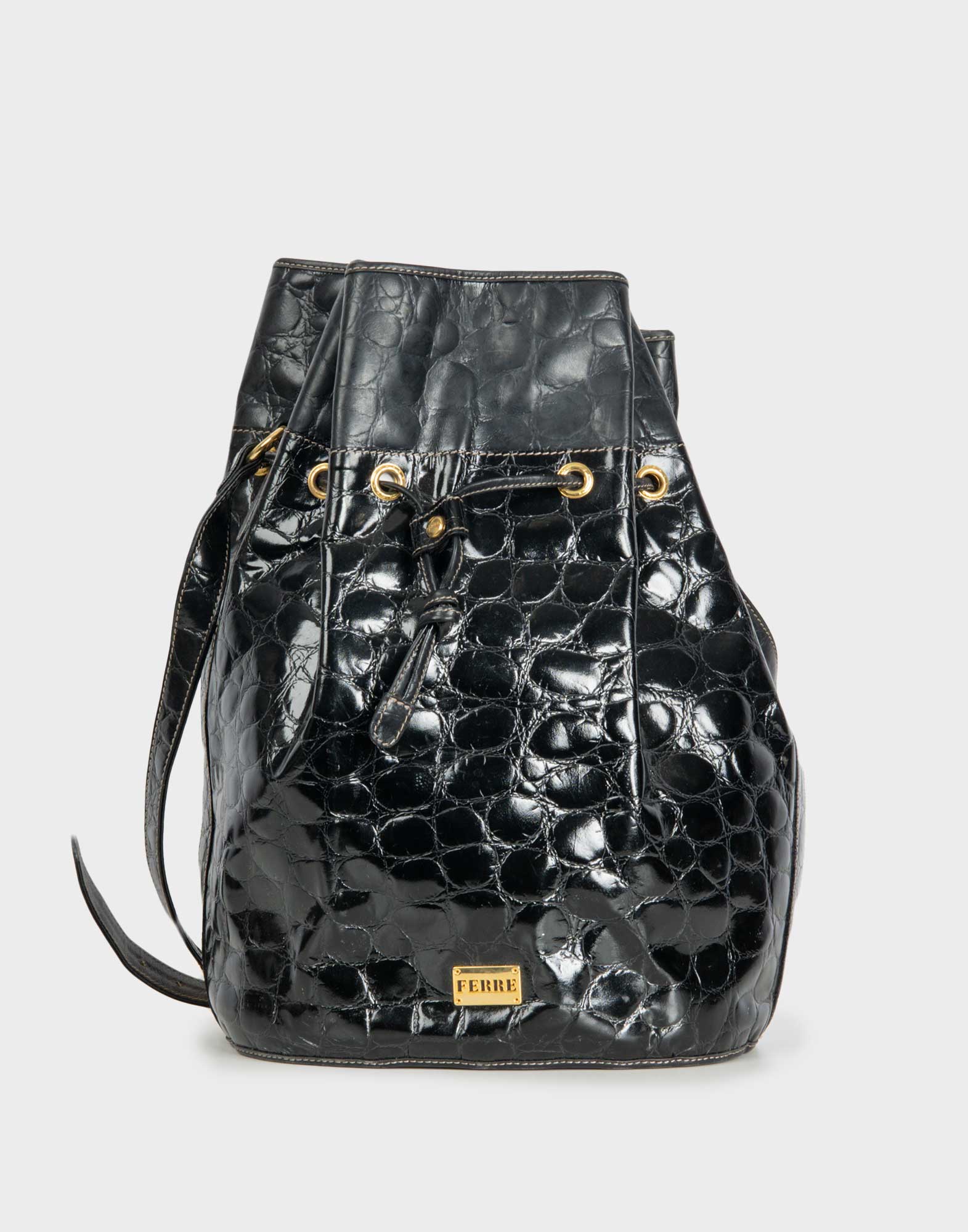 Una borsa a secchiello di Ferre in pelle nera lucida con una texture che imita la pelle di coccodrillo è presentata frontalmente. La borsa ha una chiusura a coulisse con lacci in pelle che passano attraverso occhielli dorati. Un manico laterale singolo è visibile sul lato sinistro. Un piccolo logo rettangolare dorato con la scritta "FERRE" è posizionato nella parte inferiore centrale della borsa.